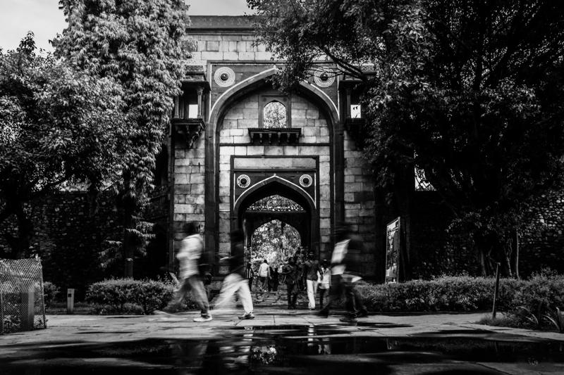 People cross the open path before the red tomb’s central gateway, their small silhouettes bringing scale to the heavy stone entrance.