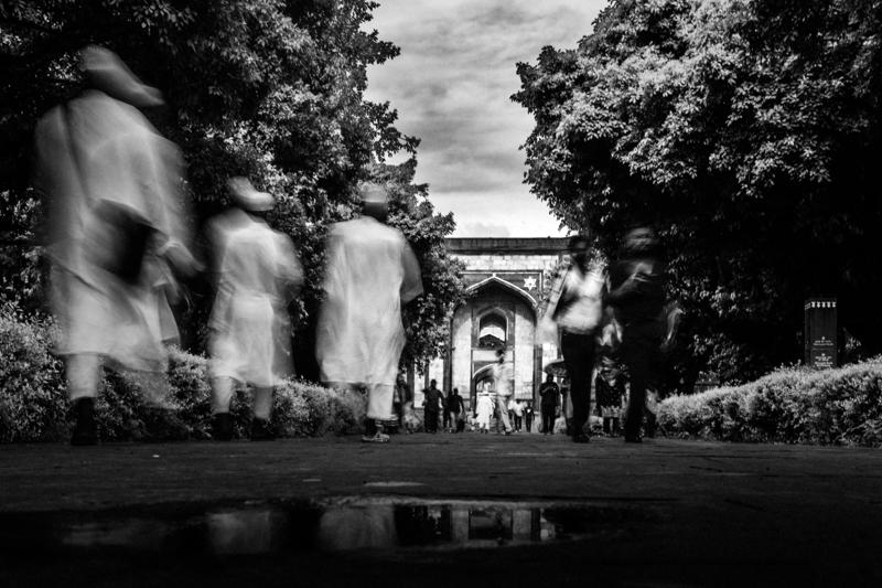 A moving figure crosses the shadowed foreground while the bright tomb remains sharp beyond the gate, setting motion against still stone.