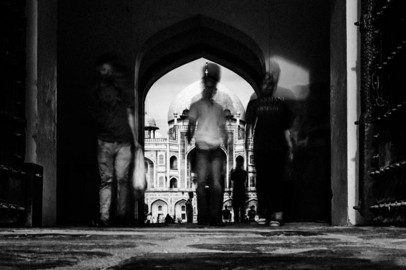 A blurred visitor passes through the arch while the pale tomb beyond remains visible, the doorway dividing shadow from open light.