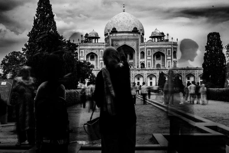 Several visitors gather in the garden before the tomb, their dark forms crossing the bright lawn and framing the central entrance.