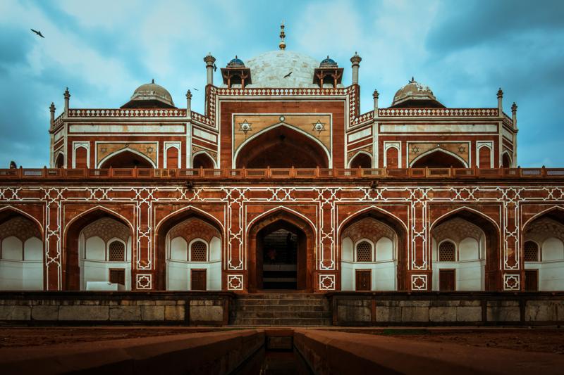 Humayun’s Tomb stands square to the camera, its red arches set against a sky and a narrow strip of green lawn.