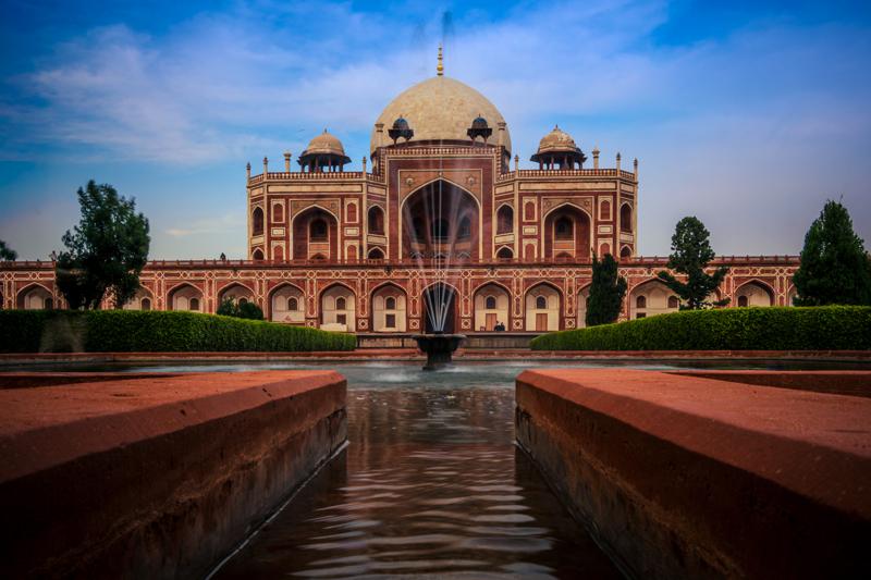 The central walkway leads toward Humayun’s Tomb while the still pool repeats its arches and trees beneath the bright sky.