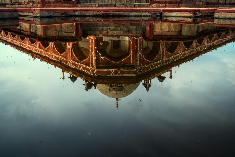 A pool reflects the sandstone arches upside down, its still waterline cutting the building cleanly across the middle of the frame.