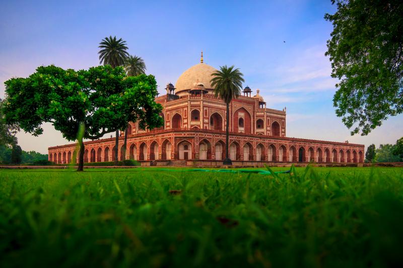Humayun’s Tomb stands beyond the lawn, its red sandstone arches balanced by palms and a clear sky in the frontal view.