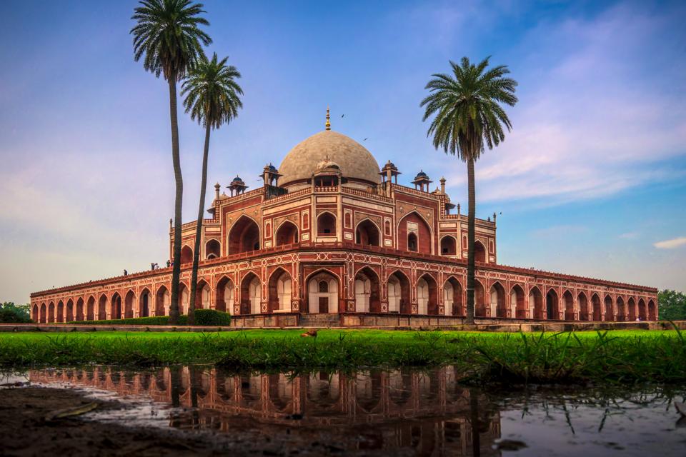Humayun’s Tomb framed by palms and reflected in still water beneath a soft evening sky in Delhi.