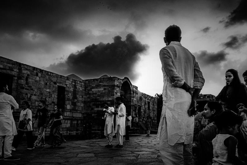 Two men pause among the old stone walls beneath Qutub Minar, their white garments bright against the dark carved surfaces.