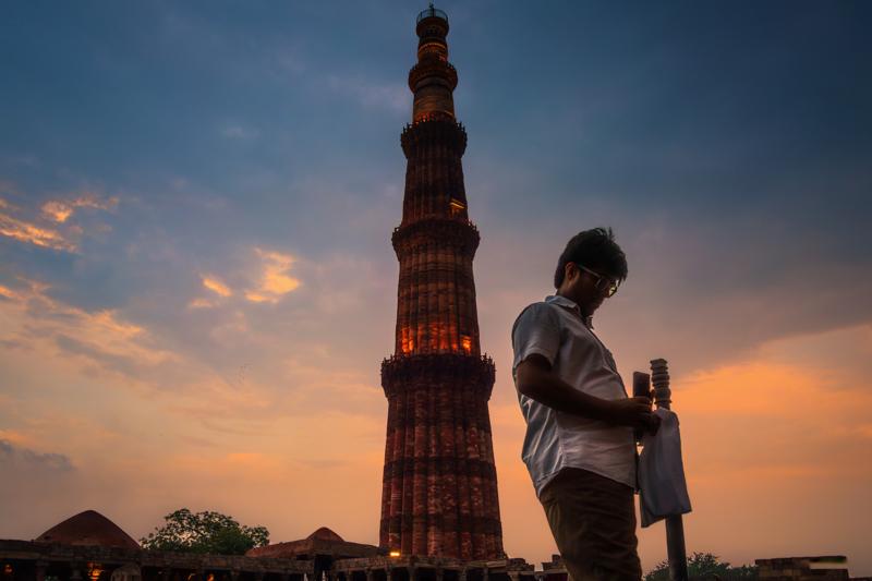 A young man checks his phone below the tower, which rises into the dusk behind him as the sky shifts to blue.
