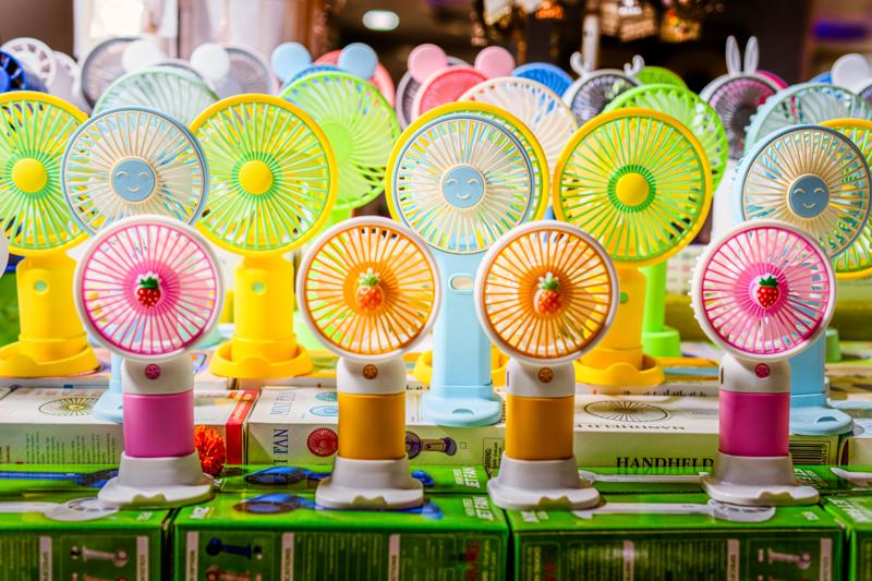 Desk fans line the shop display in repeated circles of pink, yellow and mint, their glossy plastic catching the warm lights overhead.