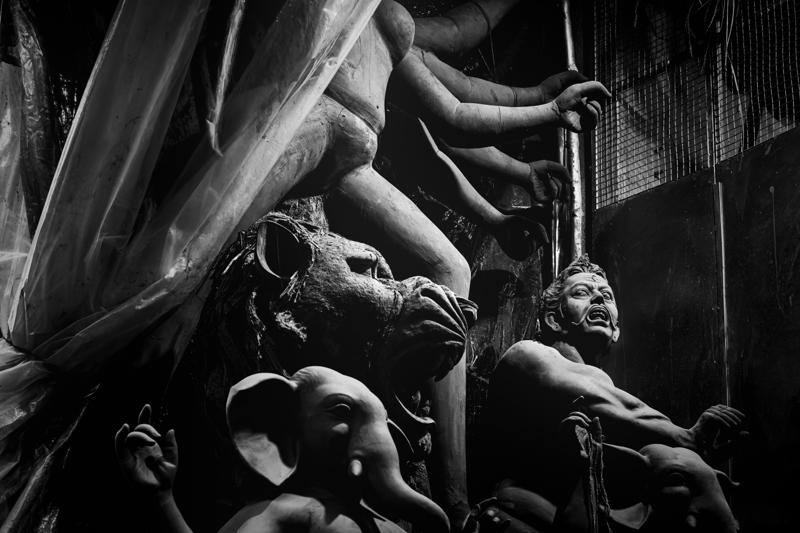 Several hands reach around a soft clay figure beneath hanging fabric, the close crop turning the workshop into a study of shapes.