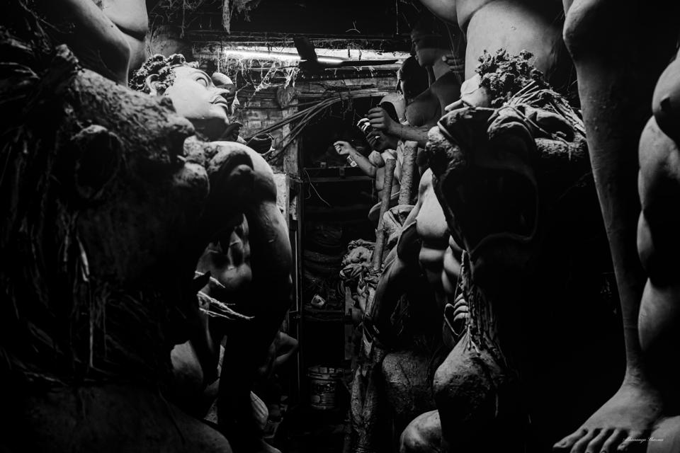An artisan surrounded by clay figures and outstretched arms inside a Kumartuli studio.