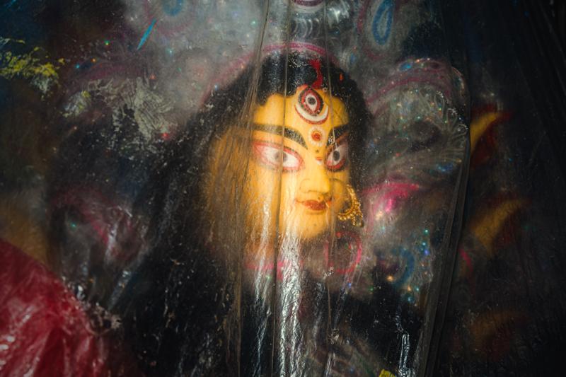 The goddess’s painted eyes meet the lens through fine ornament and reflective cloth, gold details catching light around her calm, composed face.