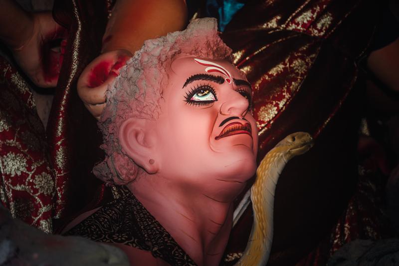 The goddess’s face fills the frame, her wide eyes lifted above the carved crown and warm red details across the sculpted ornament.