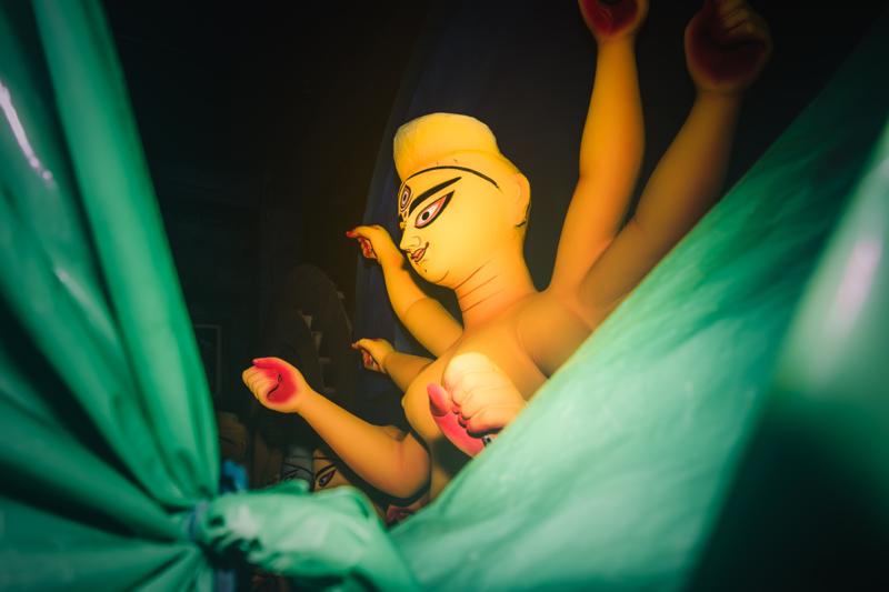 The unfinished idol’s face emerges from a ring of sculpted arms, each pale limb caught by the soft light in the room.