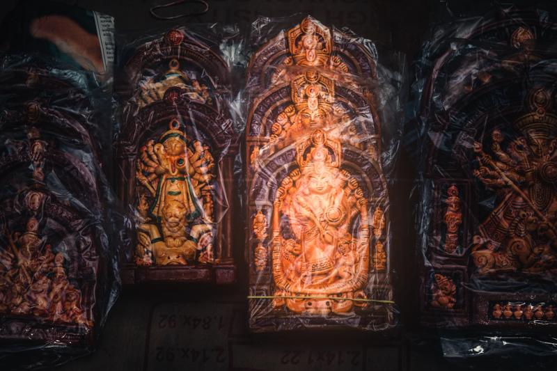 A richly coloured Durga face looks out from the pandal wall, framed by painted figures and warm spots of reflected light inside.