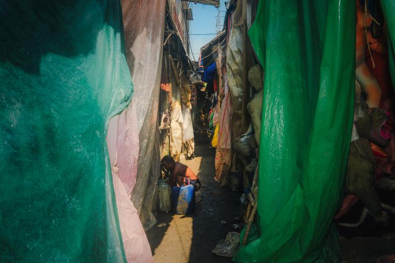 Green cloth narrows the passage between unfinished figures, drawing the eye toward a worker at the far end of the sculptor’s workshop.