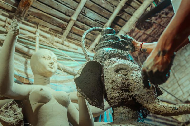 Rows of pale bodies lie under curved bamboo supports, their smooth limbs repeating across the crowded workshop ceiling, nearby, under workshop light.