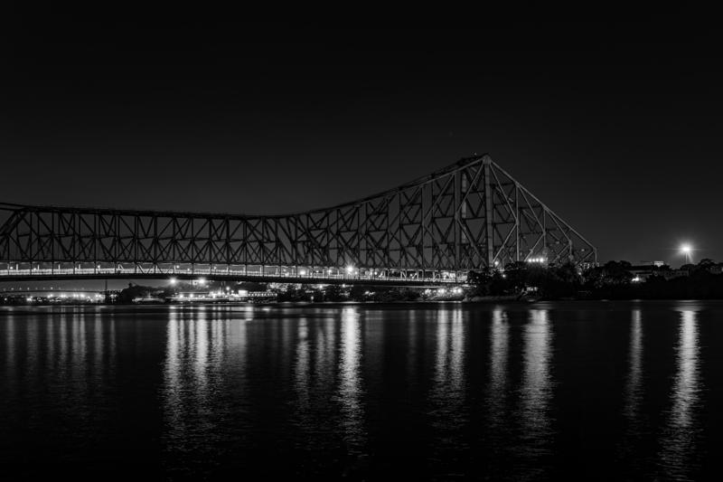 White lights trace the steel bridge above clear still water, while its unbroken monochrome reflection doubles the steelwork beneath the black night sky.