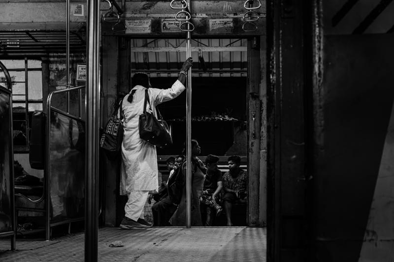 A man stands in the narrow doorway beneath suspended goods, his figure framed by shelves and the passage behind him.