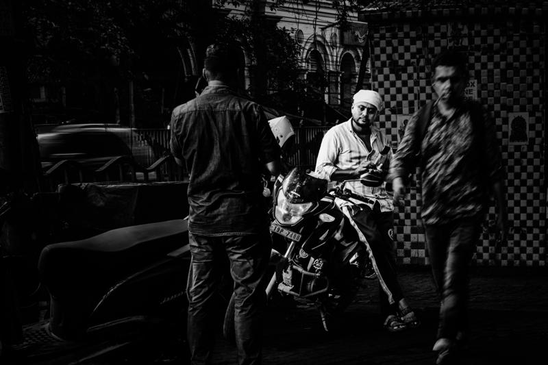 Three men occupy the shopfront, one turning toward the lens as others work behind him among hanging goods and shadow.