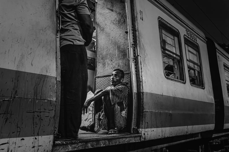 A man climbs aboard the train with a bundled load, the open doorway framing his movement against the railway platform.