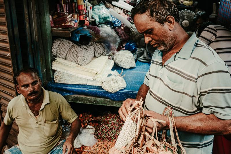 A man handles fabric inside the shop while folded cloth fills the foreground, the narrow opening enclosing his working posture.