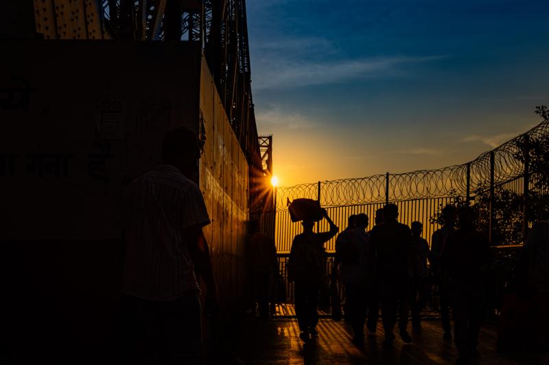 People move between the market walls as the sun shines directly through the passage, turning each figure into a silhouette.