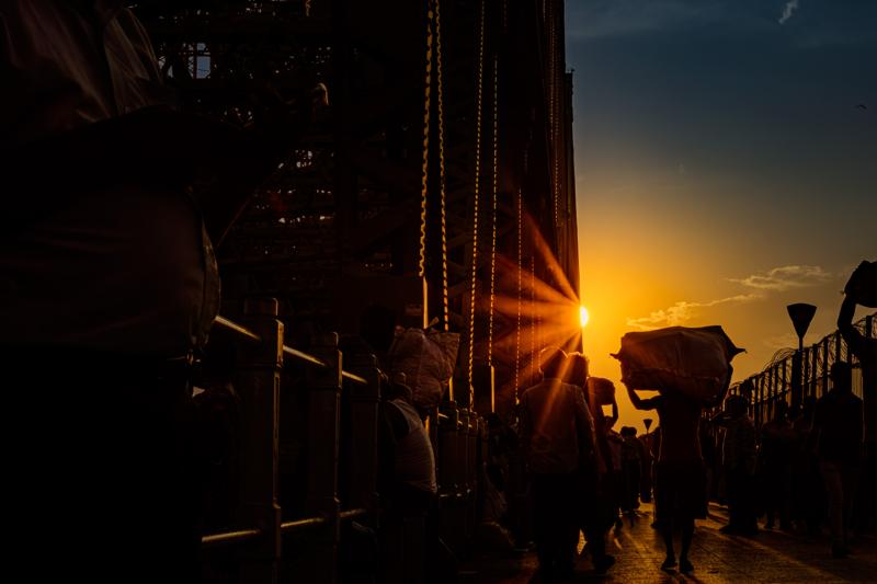 A flare cuts through the market street as people pass stalls and painted walls, their figures softened by the backlight.