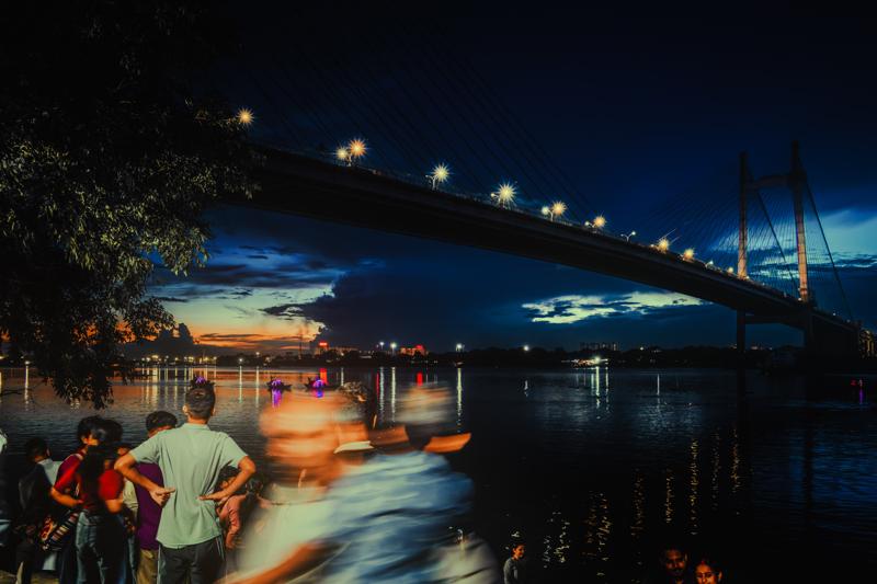 Blue hour settles over the bridge while blurred visitors gather along the bank, their movement softened against the crisp lights and dark water.