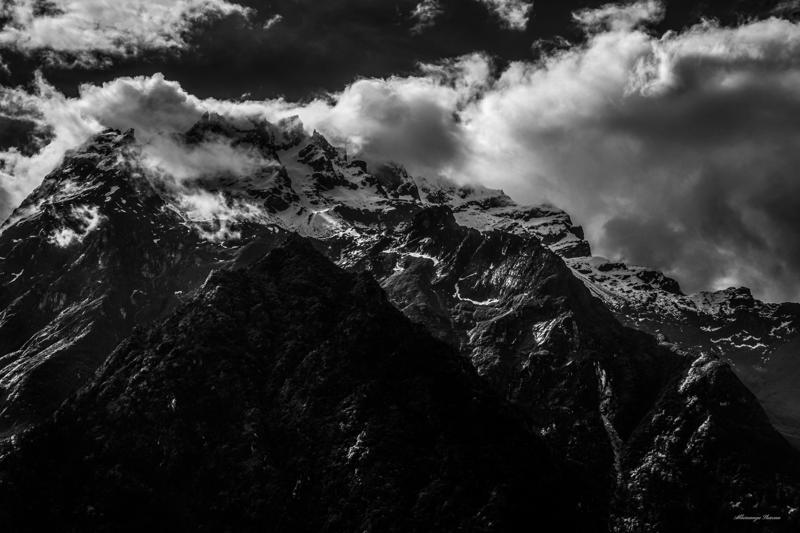 Dark mountain spires rise through shifting cloud, with the high ridge occupying the frame beneath a bright, broken sky.
