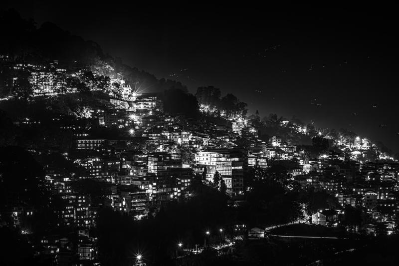 A hillside town glitters against the night, each cluster of lights tracing the slope beneath the deep, nearly black sky.