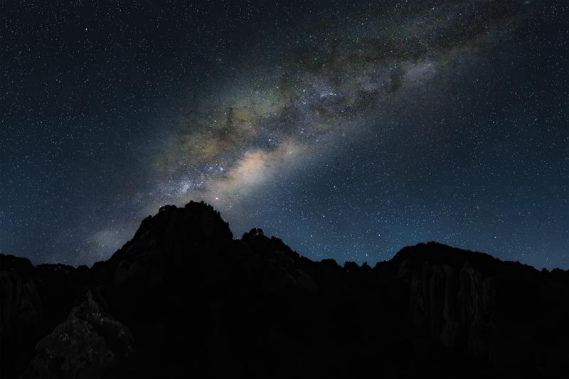A dense sweep of stars rises above the jagged ridge, with the mountain silhouette keeping the galactic band in the frame.