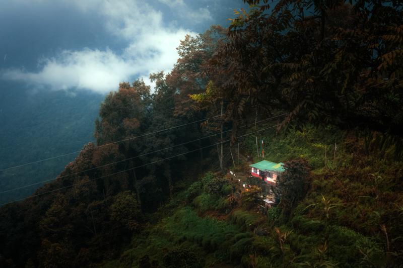 One small house sits among dark trees on the hillside, with cloud veiling the surrounding ridges and softening the distance.