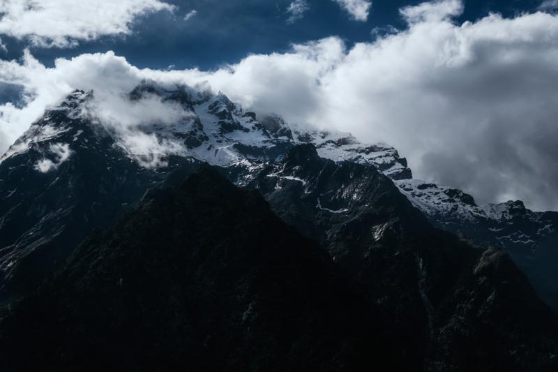 Rugged mountains hold the lower frame as thick white cloud breaks above the ridge and spills into the valley below.