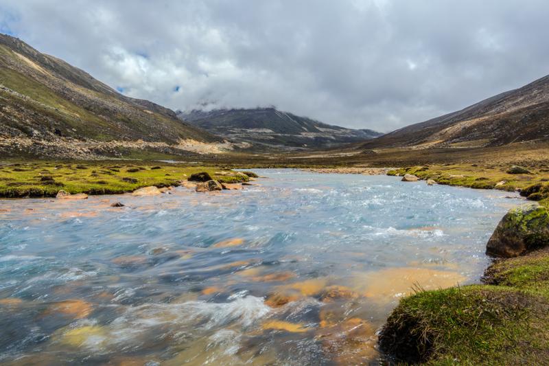 A weathered beam frames the river and grassy valley, bringing the clear water close while the hills recede into light.