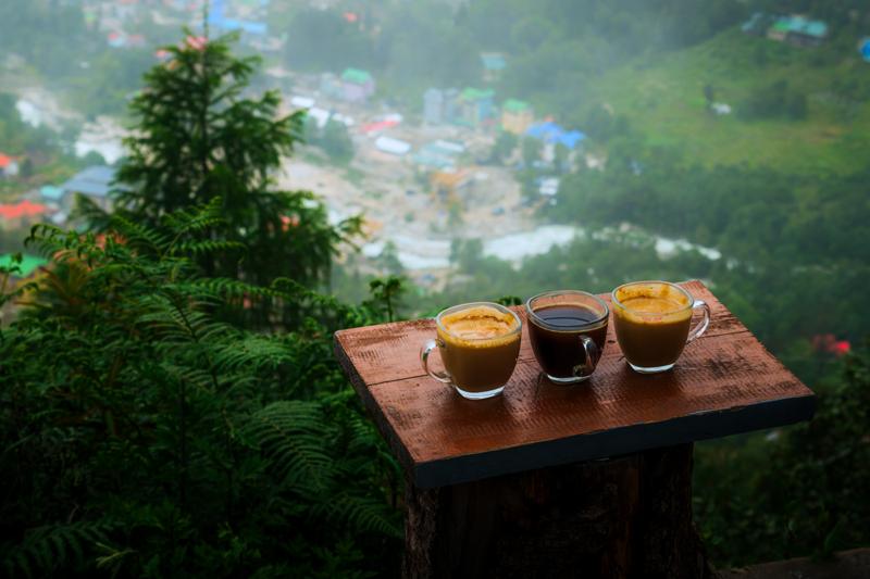 Three cups rest on a wooden table before the misty hillside, their warm brown surface set against the soft green distance.