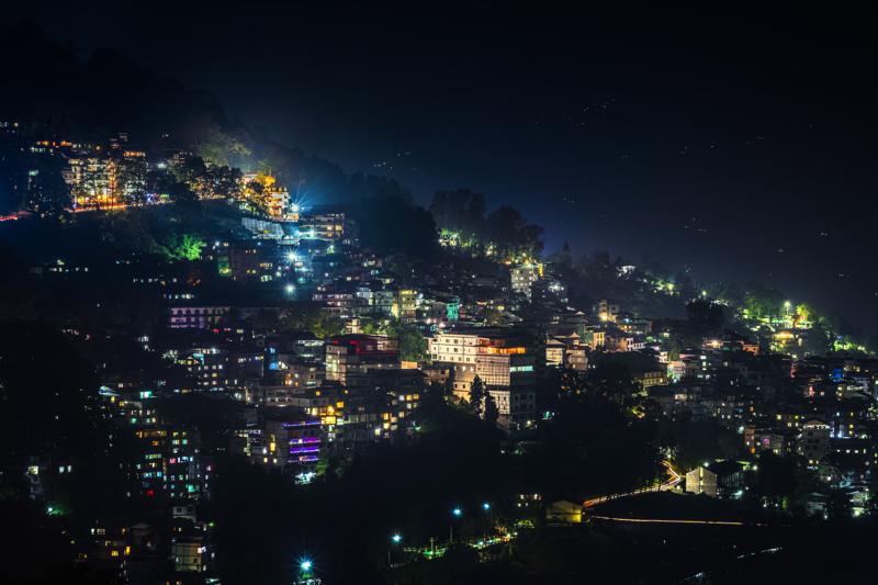 Scattered windows trace the steep town through darkness, the cluster near the centre and forested slopes fading at the edges.