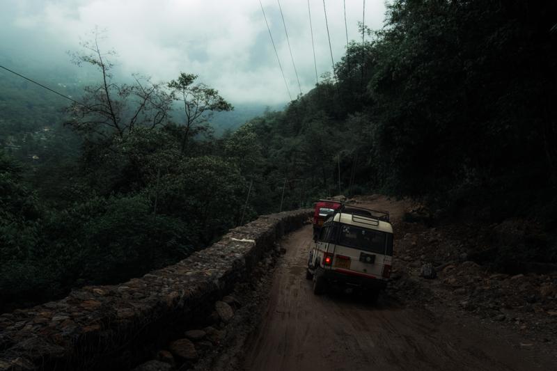Headlights approach along wet mountain road as fog closes over the trees, leaving the bus as the scene’s only point.
