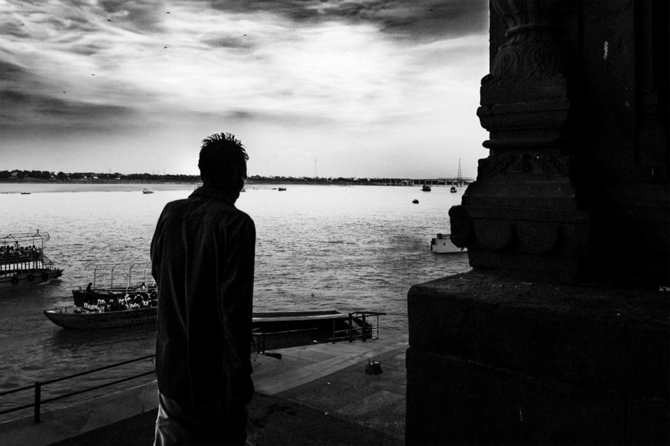 A person stands facing the water beside a dark stone structure.