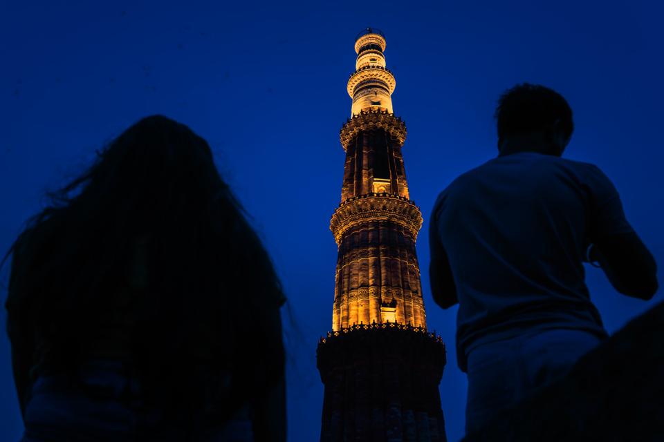 A lit tower rises above two silhouetted people in the evening.